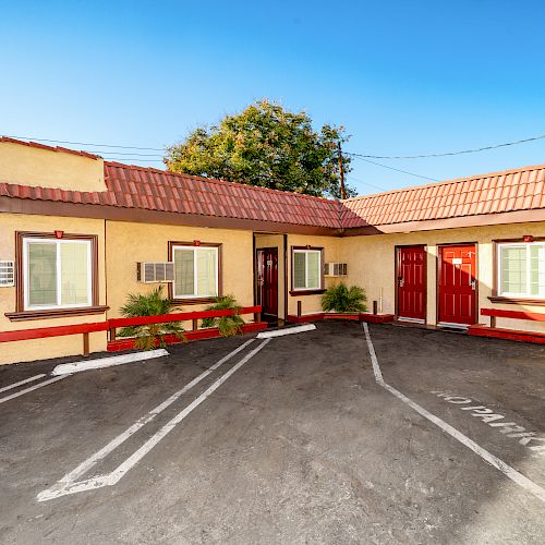 The image shows an outdoor view of a small motel or apartment complex with red doors, air conditioning units, and parking spaces in front.