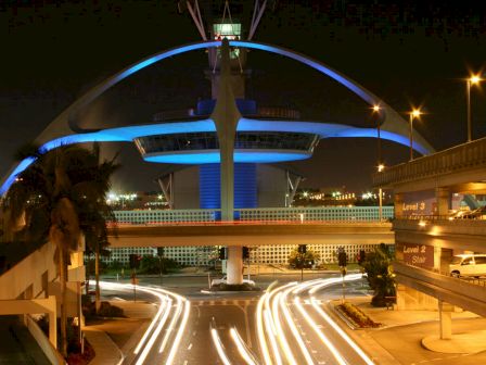 A futuristic structure with a blue glow is surrounded by light streaks from moving vehicles at night near a parking structure labeled Level 3.