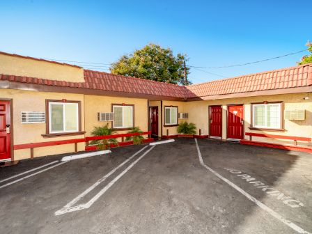 The image shows a small motel or apartment building with red doors, a paved parking area, and clear, sunny skies ending the sentence.